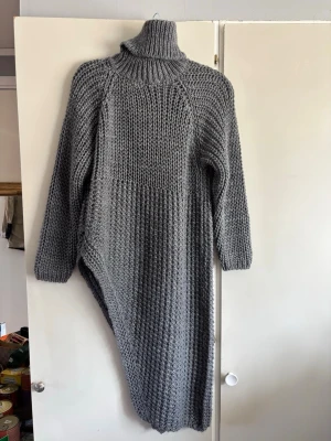 Grå stickad poloklänning - Mysig och chunky grå stickad klänning med polokrage och lång ärm. Grovstickad struktur och avslappnad passform som ger en cool oversized look. Perfekt för lager på lager och höstmys. Materialet känns mjukt och värmande.
