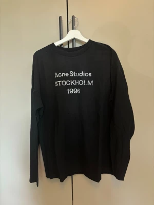 Svart långärmad Acne Studios t-shirt - Snygg svart långärmad t-shirt från Acne Studios med tryck på bröstet där det står 'Acne Studios STOCKHOLM 1996'. Klassisk rund hals och relaxed fit. Perfekt till jeans eller under en jacka.                                Använd någon gång endast! Har ej kvitto! 