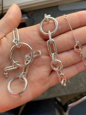 Silver platerat set från pilgrim - Aldrig använda smycken från pilgrim med original asken kvar, ett halsband med matchande örhängen i silverfärgad/ silverplaterad metall. Mycket fint skick, örhängena har fått lätta fläckar på sig förmodligen pga pappret de legat i, men med lite puts tror jag att det försvinner direkt.