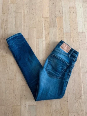 Jack&jones slimfit/tim - Snygga blå jeans med slim passform och coola slitningar på benen. Jeansen har klassisk femficksdesign och en läderpatch bak i midjan. Perfekta för en avslappnad och trendig look.