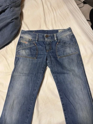 Blå jeans med broderade bakfickor - Snygga blå jeans med slitningar och unika broderade detaljer på bakfickorna. Jeansen har raka ben, framfickor. Äkta lowrise vintage disel jeans! 