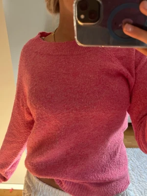 Rosa stickad tröja med rund hals - Mysig rosa stickad tröja med rund halsringning och långa ärmar. Tröjan har en enkel och klassisk design med ribbstickade muddar vid hals, ärmslut och nederkant. Perfekt för att hålla värmen under kyliga dagar.