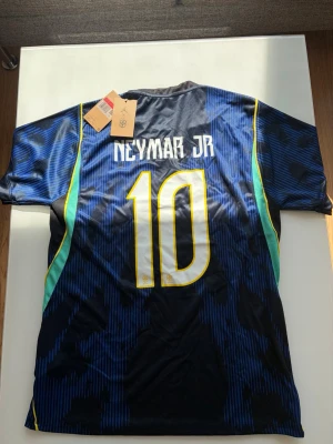 Brazil Neymar Jr - Snygg blå matchtröja från Brasilien med Neymar Jr och nummer 10 på ryggen. Tröjan har gula och turkosa detaljer, CBF-logga och Jordan-logga på bröstet. Tillverkad i lätt och ventilerande material, perfekt för fotboll eller träning.