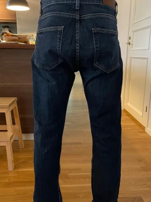 Mörkblå raka jeans herr - Säljer ett par mörkblå jeans med rak passform och klassiska bakfickor. Jeansen har normal midja och är tillverkade i denim med tydliga sömmar. Perfekta för en avslappnad och stilren look.