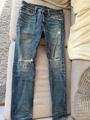 Blå slitna jeans med hål - Säljer ett par blå Ralph Lauren jeans med slitningar och hål på knäna. Jeansen har en klassisk femficksmodell, raka ben och tydliga slitdetaljer både fram och bak. Perfekta för en avslappnad och trendig streetstil. 31/32. PRIS KAN DISKUTERAS!!!
