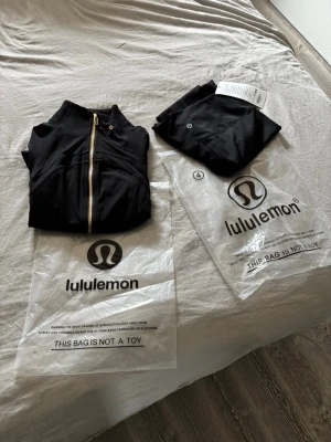 Svarta leggings från Lululemon - Snygga svarta leggings från Lululemon med diskret logga på benet. Tillverkade i ett stretchigt och mjukt material som sitter skönt och följer kroppens rörelser. Perfekta för träning eller chill. Klassisk och stilren design.