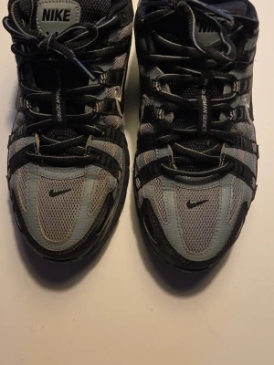 Nike P-6000 svarta och grå sneakers - Nike P-6000 sneakers i svart och grå mesh med svarta detaljer och vita loggor. Skorna har en sportig siluett med flera lager av syntetmaterial och mesh för bra andningsförmåga. Klassisk snörning och låg profil. Perfekta för dig som gillar retrovibbar och streetwear.