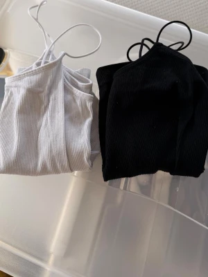 2-pack ribbade linne-toppar - Säljer två ribbade linne-toppar i svart och vitt. Båda har smala axelband och är tillverkade i mjuk bomullsmix. Perfekta att styla med jeans eller kjol för en enkel och clean look.