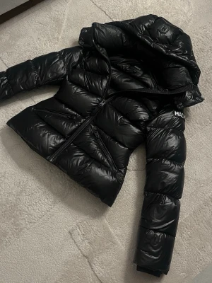 Mackage Pufferjacka XS – Äkta, Glansig & Fint Skick  - Trendig och stilren pufferjacka från Mackage i storlek XS. Jackan är glansig, varm och har en snygg, figurnära passform. Användes som vinterjacka under slutet av 2024 och början av 2025, men har sedan dess inte kommit till användning. Den är i jättebra skick utan några skador eller fel. Jackan är äkta och kvitto finns i slutet på annonsen. Ordinarie pris är 10 200 kr. Priset kan diskuteras vid seriöst intresse!
