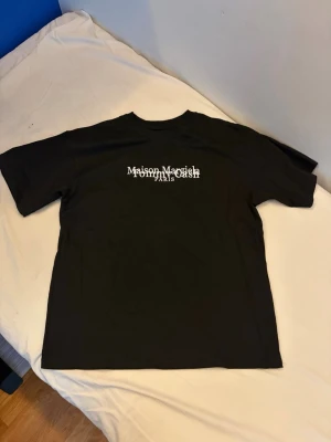 Maison Margiela t-shirt x Tommy cash - Cool  t-shirt med  Maison Margiela x Tommy cash Paris-logga på bröstet. Klassisk passform med rund hals och korta ärmar. Perfekt för dig som gillar streetwear och vill sticka ut med en unik design.