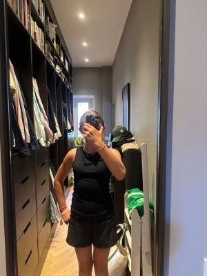 Svart ribbad linnetopp - Säljer en svart ribbad linnetopp med tight passform och ärmlös design. Perfekt att styla till både jeans och kjol. Materialet känns mjukt och stretchigt, vilket gör den superbekväm att bära. Enkel och clean look som funkar till allt.