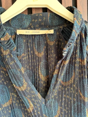 Mönstrad blus från Danska  Rue de Femme - Snygg mörkblå blus från Rue de Femme med abstrakt mönster i blått och brons. Blusen har v-ringning, tunna plisserade detaljer. 