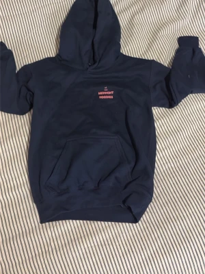 Mörkblå hoodie med leopardstjärna - Snygg mörkblå hoodie med huva och känguruficka. På bröstet står det 'Midnight Hoodies' i rött och vitt, och på ryggen finns en stor stjärna med leopardmönster. Perfekt för dig som gillar unika detaljer och streetstyle.