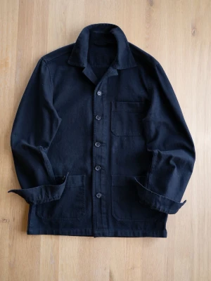 Black Chore Jacket, size M - Stilren svart overshirt i kraftigt tyg med klassisk krage och knäppning framtill. Tre fickor framtill, varav en bröstficka och två större nedtill. Perfekt lager på lager-plagg för en avslappnad look.