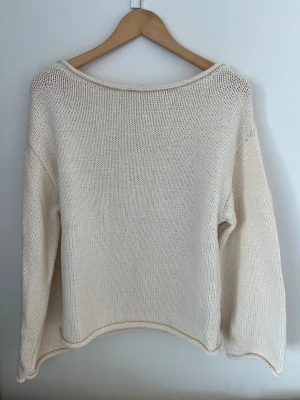 Krämvit stickad tröja - En enkel och stilren krämvit stickad tröja med avslappnad passform och långa ärmar. Tröjan har en bred, rund halsringning och raka kanter. Perfekt att matcha med jeans eller kjol för en clean look. Använd en gång