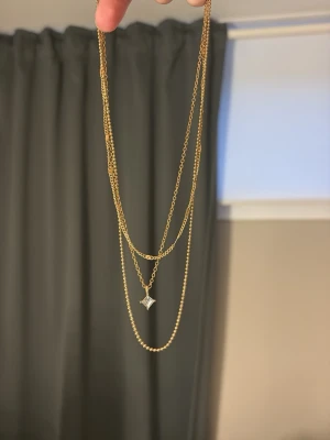 Guld halsband  - Snyggt halsband i guldton med två tunna kedjor i olika längder. Den ena kedjan har en liten diamantformad berlock i genomskinlig sten som ger en elegant touch. Perfekt för att lyfta vilken outfit som helst.