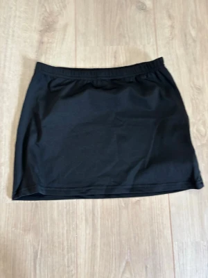 Svart kortkjol från SHEIN - En enkel och stilren svart kortkjol från SHEIN i stretchigt material. Kjolen har en rak passform och resår i midjan för extra komfort. Perfekt att matcha med olika toppar för en trendig look.