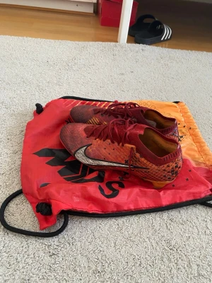 Röda Nike Mercurial fotbollsskor - Säljer ett par röda Nike Mercurial fotbollsskor med svart och silverfärgad swoosh. Skorna har snörning, låg profil och mönstrad ovandel för bra grepp på planen. Perfekta för dig som vill ha stil och prestanda på fotbollsplanen.