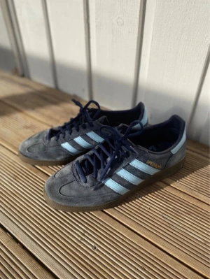 Adidas Spezial gråblå sneakers - Säljer ett par Adidas Spezial sneakers i mörkgrå mocka med ljusblå ränder och mörkblå snören. Skorna har klassisk låg profil och gummisula med Adidas-logga undertill. Perfekta för dig som gillar retrostil och streetwear.