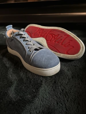 Blåa sneakers från Christian Louboutin - Snygga blåa sneakers i mocka från Christian Louboutin med klassisk röd sula och vita kanter. Skorna har rund tå, matchande blå skosnören och diskret branding på sulan. Perfekta för dig som vill sticka ut med exklusiv stil. Bara använda ett fåtal gånger.