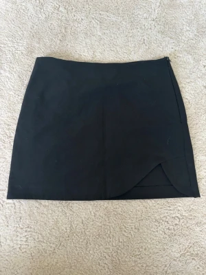 Svart kjol med slits - Fin stilren kjol med slits, dragkedja på sidan, inte stretchigt material, har används fåtal gånger med köpte på plick så vet ej hur många gånger den är använd sen innan