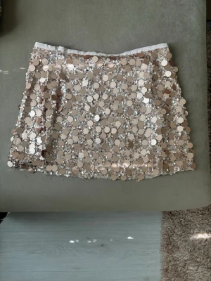 Ny Zara paljettkjol - Kort kjol i beige med stora, glittriga paljetter över hela tyget. Kjolen har en rak passform och ger ett riktigt statement-utseende. Perfekt för dig som vill sticka ut och glänsa lite extra.