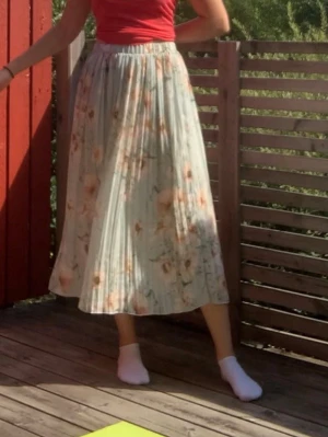 Ljusblommig plisserad långkjol - Säljer en ljus, plisserad långkjol med blommigt mönster i pastellgrön. Kjolen har en mjuk och flowy känsla, perfekt för varma dagar. Resår i midjan för skön passform och ett romantiskt uttryck.