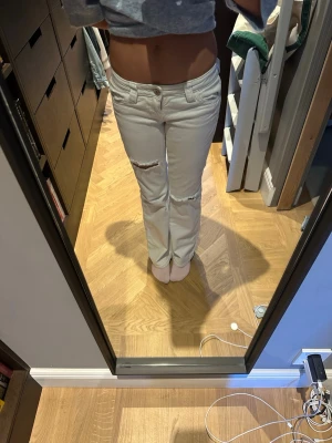 Vita raka jeans med slitningar - Säljer ett par vita jeans med raka ben och slitningar vid knäna. Jeansen har klassisk femficksmodell och normal midja. Perfekta för en avslappnad och trendig look.