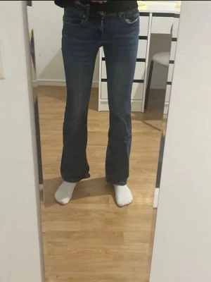 Blå bootcut jeans med låg midja - Säljer ett par klassiska blå bootcut jeans med låg midja och fem fickor. Jeansen har en lätt utsvängd passform nedtill och är i ett mjukt denimtyg. Perfekta för dig som gillar en retroinspirerad look.