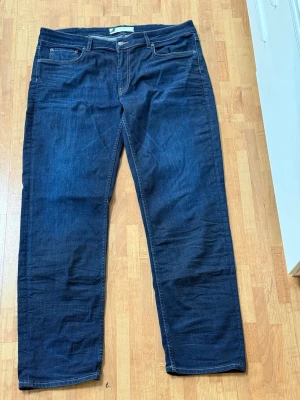 Mörkblå raka jeans - Snygga mörkblå jeans med rak passform och klassisk femficksdesign. Jeansen har kontrastsömmar och är tillverkade i ett mjukt denimtyg som ger en avslappnad look. Perfekta till en enkel t-shirt eller hoodie.