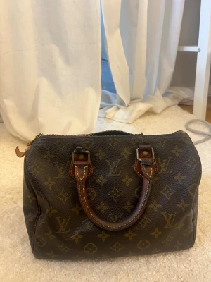 Louis Vuitton Speedy 25 väska  - Louis Vuitton väska i den gamla speedy 25 modellen. Är väldigt sliten men har limmat och sytt ihop där handtagen sitter då alla gått av. Den går att använda men kan säkert gå upp igen. Säljer då jag inte har orken att lämna in den till en skomakare eller något liknande. Så nu får någon annan som orkar ta hand om den göra de eller ha den som den är nu💕 Den är äkta som man kan se på detaljerna, som till exempel Louis Vuitton trycken på lappen och dragkedjan och koden på insidan. Skriv för mer info