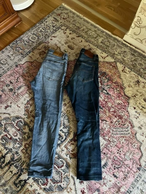 2 Tiger of sweden jeans - Säljer två par jeans i olika blå tvättar, ett par ljusblå och ett par mörkblå. Båda har klassisk femficksdesign, raka ben och normal midja. Perfekta för en avslappnad och trendig look. Materialet är denim med snygga detaljer och kontrastsömmar.