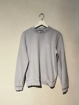 Lacoste tröja - Tröja från Lacoste i ljus blå färg, köpt på zalando för 2 år sedan, har legat orörd senaste året pga storleken, storlek S men kan förekomma större än normalt