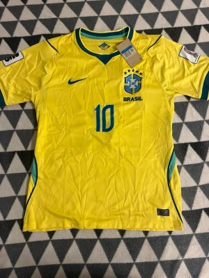 Brasilien fotbollströja  - Fotbollströja i storlek M med Neymar tryck på baksidan, gul färg med Brasiliens logga på framsidan. Skön att ha på sig både hemma och ute. Man kan ha den som vanlig tröja och träningströja 