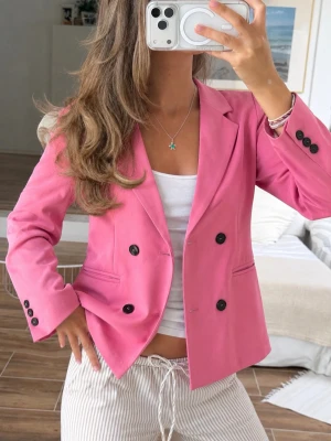 Rosa kavaj från Gina Tricot - Trendig rosa kavaj från Gina Tricot i dubbelknäppt modell med svarta knappar. Klassisk krage och två fickor framtill. Perfekt för dig som vill sticka ut med färg och ha en snygg, modern look. Materialet känns mjukt och följsamt.