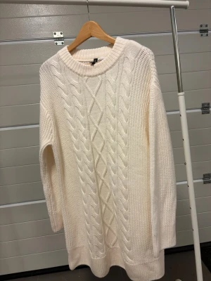 Vit kabelstickad tröja/klänning Divided - Mysig vit kabelstickad klänning (eller lång tröja) från H&M Divided. Oanvänd! Tröjan har ett klassiskt flätmönster framtill, rund halsringning och långa ärmar. Perfekt för lager på lager och en clean look till jeans eller tights.