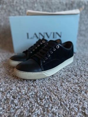 Lanvin cap toe - Hej! Just nu säljer jag dessa lanvin cap toe i storlek 41 som håller ett mycket bra skick! Ända defekten är att hällen i ena skon har gått upp och tillfälligt lagats med skoplåster. Detta kan självklart förbättras bättre på annat sätt! Utöver det är skorna i mycket bra skick och har dessutom blivit utrustade med nya snören. Tåboxen och mockan är i stabilt och fint skick. Ingår: Box, dustbag och extra snören! Skorna kan definitivt passa någon med storlek 42. Hör av er vid minska fråga!🤗MVH: Kings