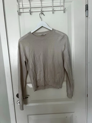 Beige stickad tröja från H&M - En enkel och stilren beige stickad tröja från H&M. Tröjan har rund halsringning, långa ärmar och ribbade muddar vid ärmslut och nederkant. 