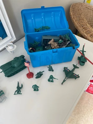 Låda med gröna plastarmésoldater - Säljer en blå plastlåda fylld med klassiska gröna armésoldater, fordon som stridsvagn, helikopter och flygplan samt tillbehör som flagga och hinder. Figurerna är i olika poser och tillverkade i hård plast. Perfekt för dig som gillar att bygga upp egna slagfält och leka strategiskt.