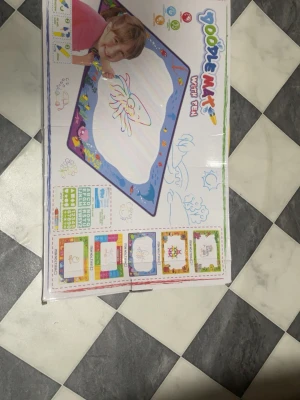 Doodle Mat vattenmålarset - Rolig Doodle Mat där du kan måla med vattenpenna på en stor matta. Mattan har färgglada kanter med olika motiv och figurer. Perfekt för kreativ lek utan kladd. Inkluderar flera mallar och tillbehör för att skapa olika bilder.