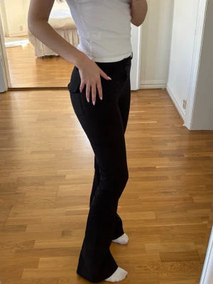 Svarta kostymbyxor med utsvängda ben - Säljer ett par svarta kostymbyxor med utsvängda ben och knappdetaljer vid fickorna. Byxorna är relativt stretchiga, ger en stilren look som passar perfekt till en trendig outfit💕💕Skriv för mer info