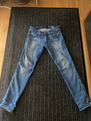 Blå slim fit jeans från replay - Snygga blå slim fit jeans från Lindex med klassisk femficksdesign och lätt slitna detaljer framtill. Har ett litet hål som ni ser på bilden, men verkligen jättelitet. Jeansen har normal midja och smala ben, perfekta för en trendig och avslappnad look. Tillverkade i bomullsdenim med lite stretch för extra komfort.