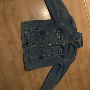 Klassisk blå jeansjacka - Snygg blå jeansjacka i klassisk modell med raka linjer och flera fickor framtill. Jackan har silverfärgade knappar och en cool, avslappnad vibe. Perfekt att slänga över en hoodie eller t-shirt för en casual look.