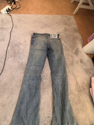 Ljusblå bootcut jeans - Säljer ett par ljusblå bootcut jeans med klassisk femficksdesign och utsvängda ben. Jeansen har en snygg tvättad look och är tillverkade i denim. Perfekta för dig som gillar retrostil och vill ha ett par jeans som sticker ut.