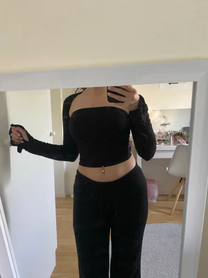 Svart croppad långärmad topp - Säljer en svart, croppad topp med lång ärm och axelbandslös design. Toppen har en tight passform och är perfekt för dig som gillar stilrena och trendiga plagg. Materialet känns mjukt och stretchigt, vilket gör den bekväm att bära.