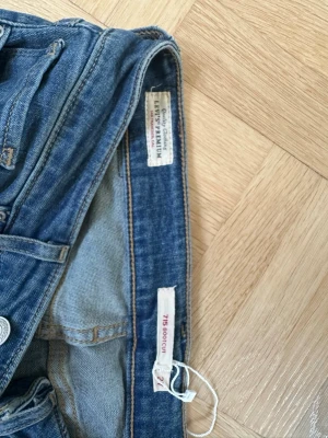 Levi's 715 Bootcut jeans blå - Ett par klassiska blå Levi's 715 Bootcut jeans i 100% bomull. Jeansen har fem fickor, knappgylf och bootcut passform som ger en snygg siluett. Perfekta för dig som gillar tidlös denimstil och vill ha ett par jeans som funkar till allt.