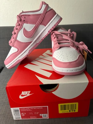 Nike Dunk Low rosa och vita sneakers NYA - Helt nya Nike Dunk Low Next Nature sneakers i en snygg rosa och vit färgkombination. Lågt skaft, klassisk rund tå och snörning framtill. Tillverkade i skinn med mjuk platt sula för skön komfort. Perfekta för dig som gillar streetstyle och vill sticka ut med färg.