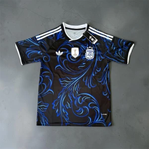 Svart-blå Argentina fotbollströja - Snygg svart fotbollströja med blått mönster och vita detaljer. Tröjan har korta ärmar, rund hals och tre vita ränder på axlarna. På bröstet finns Argentinas landslagsemblem och FIFA-märke. Perfekt för dig som älskar fotboll och vill sticka ut på planen.