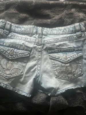🩵 Jeansshorts med broderade fickor | XS | Y2K - Säljer ett par supersnygga ljusblå jeansshorts med fina broderade detaljer på bakfickorna. De passar XS och har en låg/mellanmidjad passform med rå fåll – perfekta till sommaren! Använda men fortfarande i fint skick. Är i storlek 146/152 men passar xxs/xs 