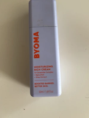BYOMA Moisturizing Rich Cream 50ml - Fuktgivande ansiktskräm från BYOMA i en ljuslila fyrkantig plastflaska med orange text. Innehåller Tri-Ceramide Complex, bakuchiol och sheaextrakt för att stärka hudbarriären och ge näring. Perfekt för dig som vill boosta huden.